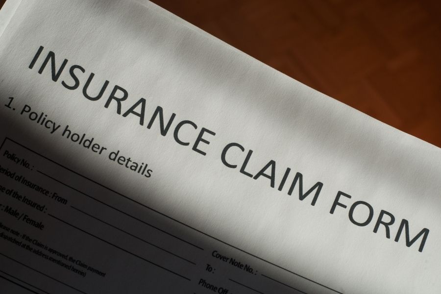Homeowner filing a property insurance claim by phone after water damage, taking notes on the timeline